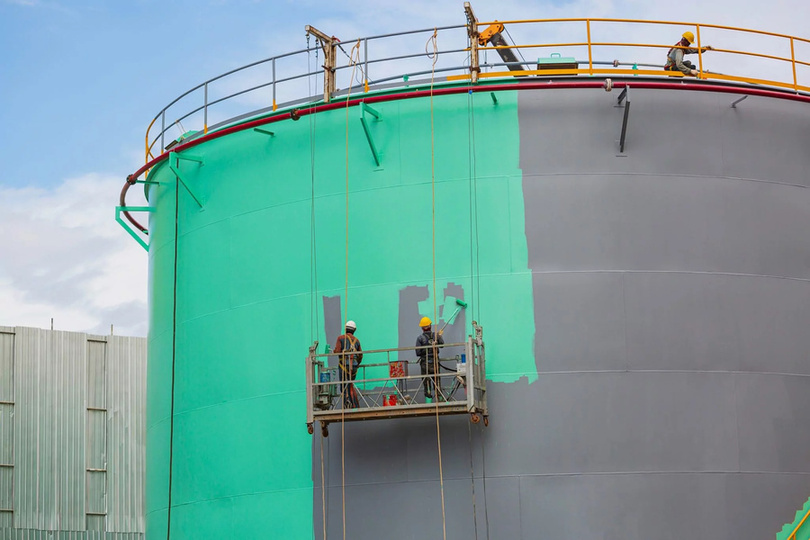 Workers applying protective coating to a large storage tank